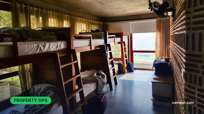 Shared hostel room with wooden bunk beds, a wall fan and a window facing the sea.